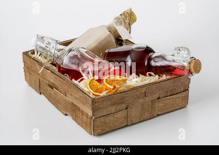 bottles with liquors in a small decorative box lined with shavings on a white background, a red apple and dried orange slices Stock Photo