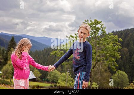 Brother and sister, siblings, boy and girl holding hands and looking angrily in the camera.Tired, not wanting to take a photo.Family vacation,mountain Stock Photo