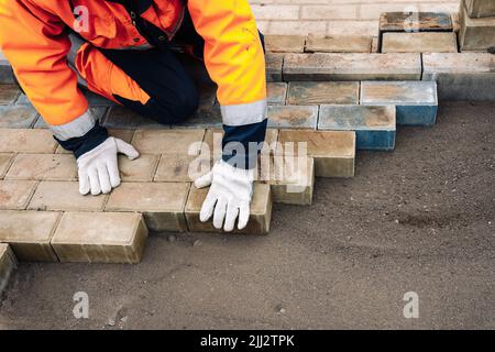 a worker in a protective work suit lays paving slabs. A professional Stock Photo