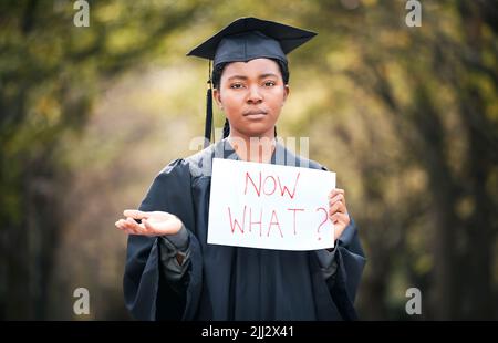 Where to from here. Portrait of a young woman holding a sign that reads now what on graduation day. Stock Photo