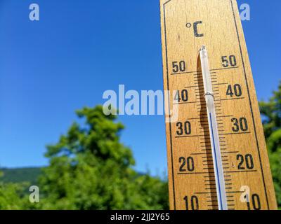 Detail of thermometer shows high temperature of over 35 in summer against trees and cloudless sky with focus on thermometer Stock Photo