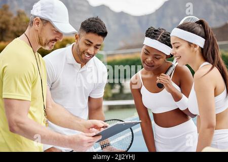 Ive worked out a strategy for all of you. a handsome mature male tennis coach using a tablet and talking strategy with his students out on the court. Stock Photo