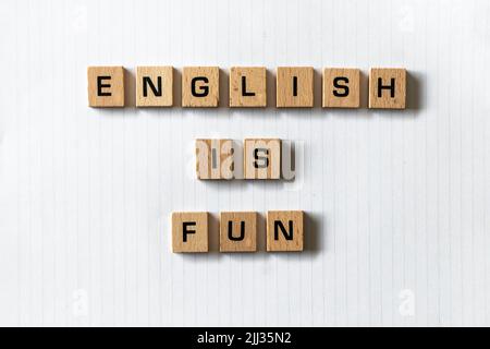 Wooden letters spell out 'English is fun' on a blank white lined notepad. Hardwood desk surface. Back to school, in-person learning, online learning. Stock Photo
