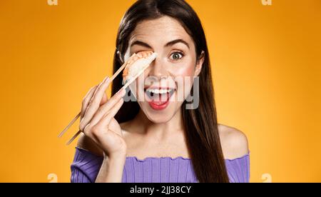 Excited girl with fresh nigiri sushi made of rise and shrimp, orange background. Stock Photo