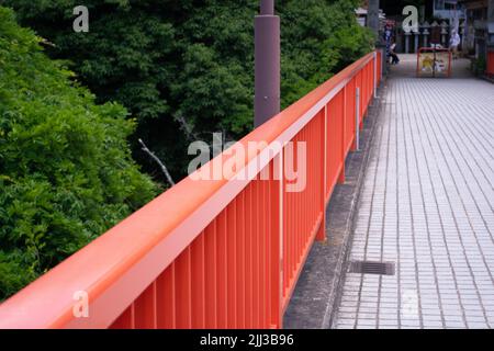 Red handrail on large pedestrian bridge over rain forest in Japan. Stock Photo