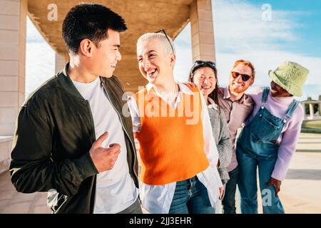 Couple of friends talking and smiling. In the back three friends smiling and having fun outdoor. Stock Photo