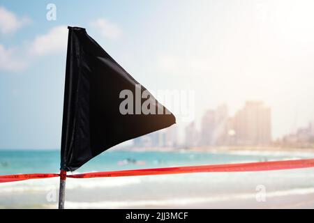 Black flag on the sea shore warning about dangerous current and waves or invasion of jellyfish. Stock Photo