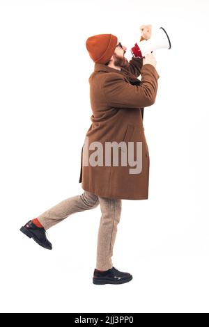 Full body shot of a stylish bearded man in a autumn coat using a loudspeaker on a white infinity background. High quality photo Stock Photo