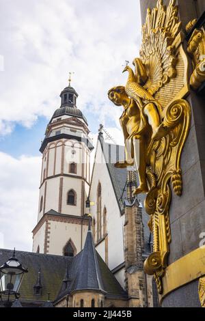 Leipzig, Germany - June 25, 2022: The the bell tower of the Thomaskirche. The golden sculpture of the Commerzbank or former Konfektionshaus Ebert blur Stock Photo