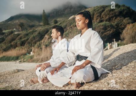Keep calm and train on. two young martial artists meditating while practicing karate on the beach. Stock Photo