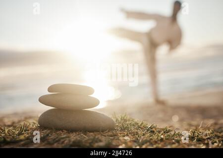 In balance there is harmony. Closeup shot of a stack of stones on the beach with a man practicing karate in the background. Stock Photo