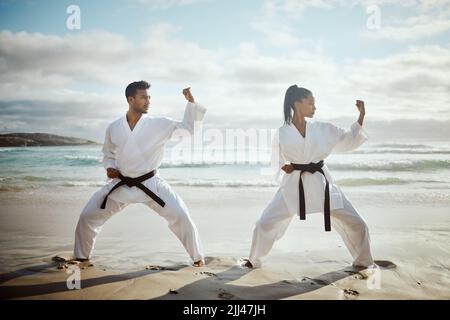 In sync. Full length shot of two young martial artists practicing karate on the beach. Stock Photo