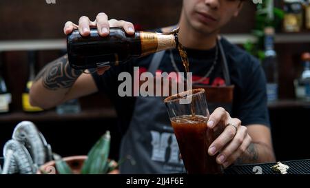 Close up of the hands of a bartender putting beer in a glass with clamato. Bartender adding beer in a glass with a red drink. Waiter at the time of preparing a drink. Stock Photo