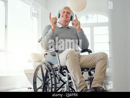 My heart still knows how to dance. an elderly man enjoying some music while sitting in the lounge at home. Stock Photo