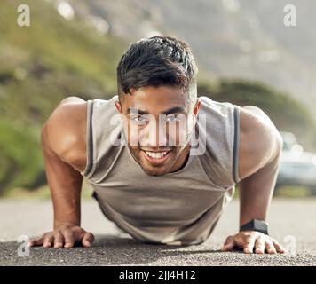 The more you do it, the more bearable it becomes. an athletic young man doing push-ups outside. Stock Photo