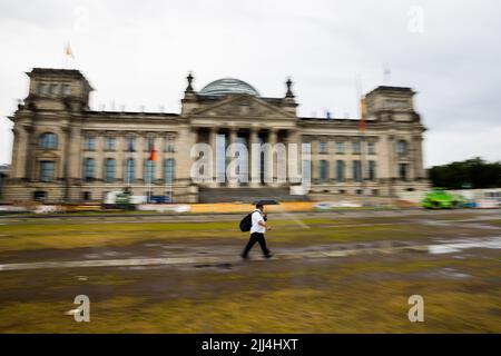 Berlin, Germany. 23rd July, 2022. A man walks in the morning with umbrella in front of the Reichstag building. (Wipe effect by pulling along) Credit: Christoph Soeder/dpa/Alamy Live News Stock Photo