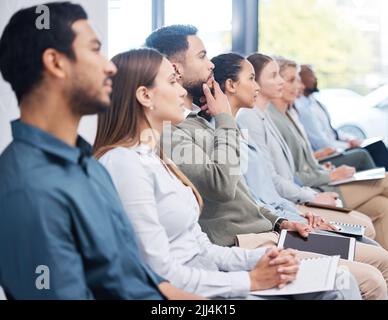 Diverse group of serious business people sitting together in office training. Focused team of colleagues using notebooks and technology while learning Stock Photo