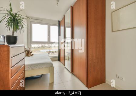 Comfortable bed with ornamental blanket placed near glass door and wardrobe with mirror in light bedroom Stock Photo
