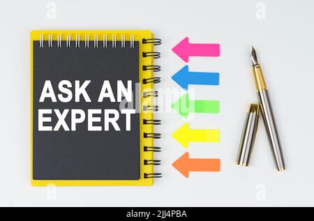 Business and finance concept. On a white background lies a pen, arrows and a notebook with the inscription - ASK AN EXPERT Stock Photo