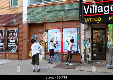 People wheatpasting advertising posters on a wall, or wild posting advertisments, as part of an street-level, guerilla, urban marketing campaign. Stock Photo