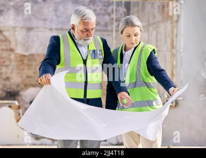 If your dreams dont scare you, they are too small. two engineers looking at blueprints while standing on a construction site. Stock Photo