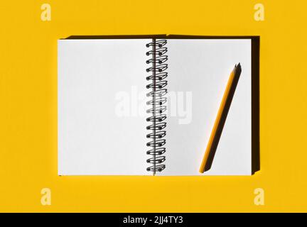 Notebook with pencil. School notebook on illuminated yellow background, spiral notepad on table. Top view of open notebook with blank pages Stock Photo