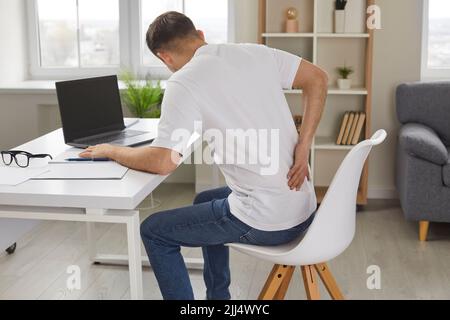 Man experiences severe back pain caused by prolonged and incorrect sitting at workplace. Stock Photo