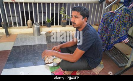 Portrait of middle aged hungry handsome man sitting on floor. Indian man with takeaway food and drinks at home Stock Photo