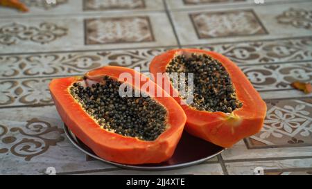 Close-up of a halved organic papaya on a plate.Ripe papaya cut in half isolated on floor background. Stock Photo