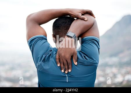 Prep your body well before you work hard. Rearview shot of a sporty young man stretching his arms while exercising outdoors. Stock Photo
