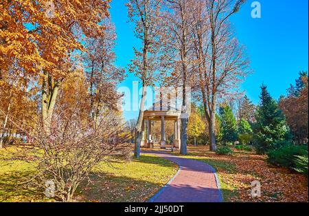 The small gazebo in park behind the tall trees with yellow-brown dry autumn foliage, Mezhyhirya, Ukraine Stock Photo