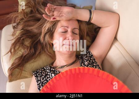 Woman lying on the sofa and suffering from the hormonal disorder of menopause with high heat. Stock Photo
