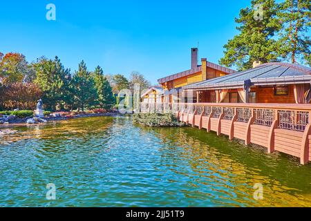 The scenic wooden bridge and small house on the lake, surrounded with lush green park, Mezhyhirya, Ukraine Stock Photo