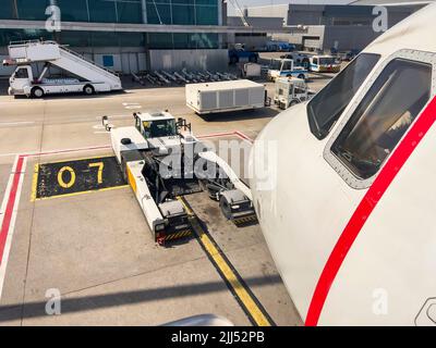 View from side of airplane cockpit on airfield with ground handling vehicles. No people. Aviation travel background with copy space. Airport gate 07 Stock Photo