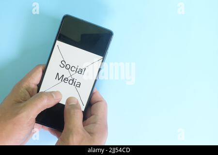 Social media and digital detox, break or pause concept. Hand holding a mobile phone with an x mark in blue background flat lay. Stock Photo