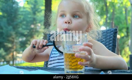 Little girl looks into the lens around. Close-up of blonde girl studying the world around her looking at it through magnifying glass while sitting in Stock Photo