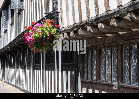 Flower basket hanging from the jettied timber framing of the Almshouses (foreground) and Guildhall, King Edward VI Grammar School. Stratford upon Avon Stock Photo