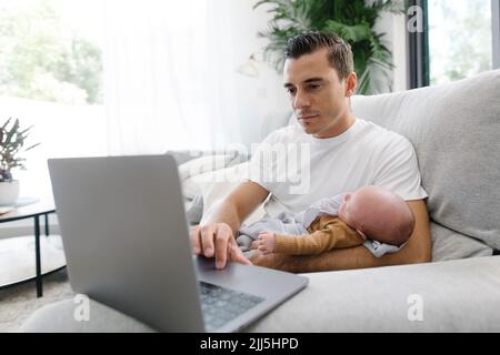 Man carrying baby in arm working from home Stock Photo