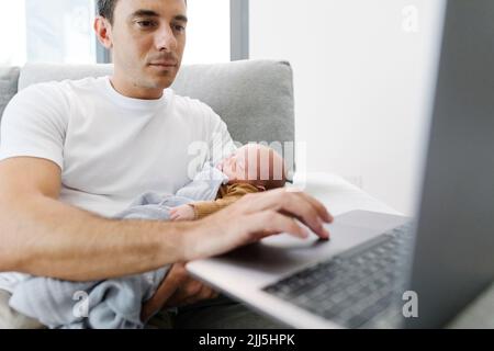 Man carrying baby in arm working from home Stock Photo