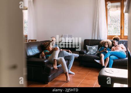 Parents looking at children using mobile phones sitting on sofa in living room Stock Photo