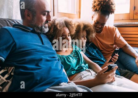 Parents looking at children using smart phones sitting on sofa Stock Photo