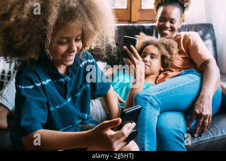 Smiling boy using mobile phone sitting by mother and sister at home Stock Photo
