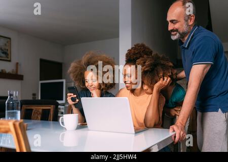 Smiling parents looking at boy using smart phone sitting at table Stock Photo
