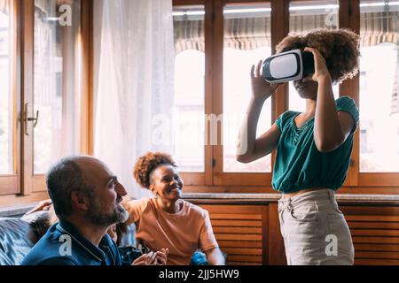 Girl wearing virtual reality simulator in front of family at home Stock Photo