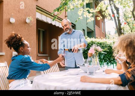 Man pouring wine into glass for woman sitting at dining table in backyard Stock Photo