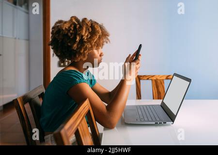 Girl sitting with laptop using smart phone at home Stock Photo