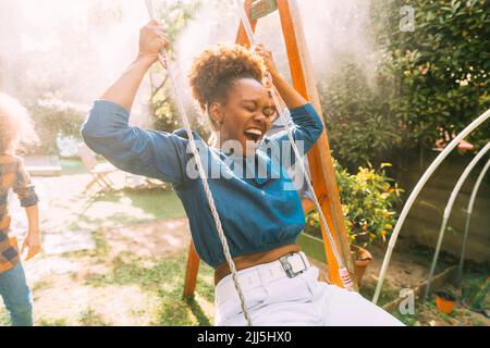 Happy woman with eyes closed swinging in backyard Stock Photo