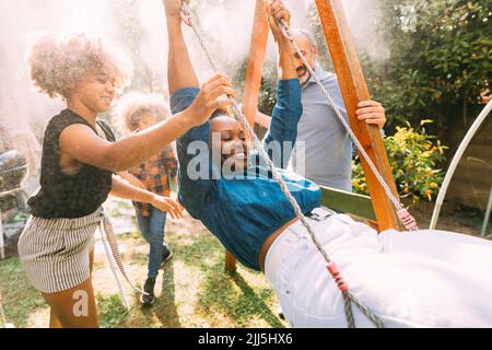 Playful woman enjoying swing with family in backyard Stock Photo