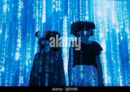 Digital code falling on boy and girl wearing virtual reality simulator Stock Photo
