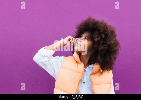 Girl with Afro hairstyle looking up against purple background Stock Photo